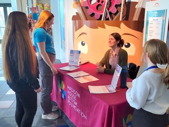 A booth that displays the name "Madison House Autism Foundation" is being surrounded by people at a conference